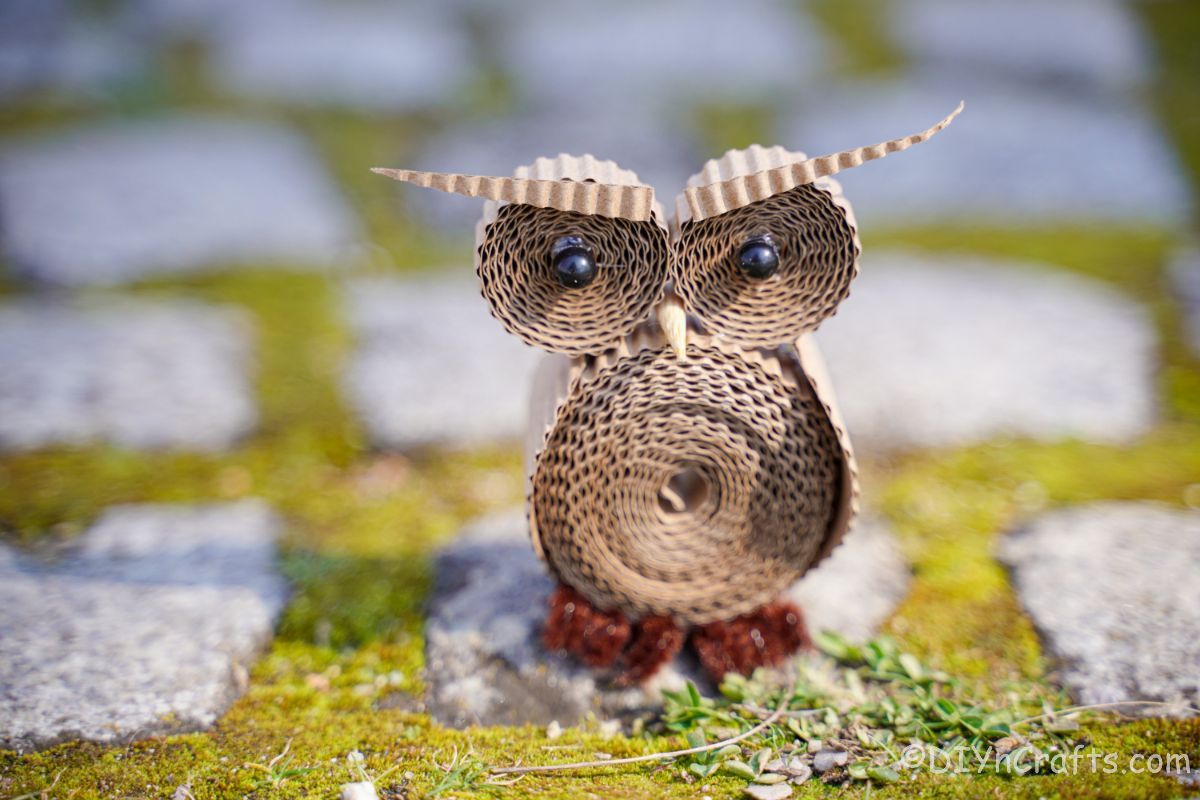 миниатюрная сова из картона на траве и каменной дорожке
