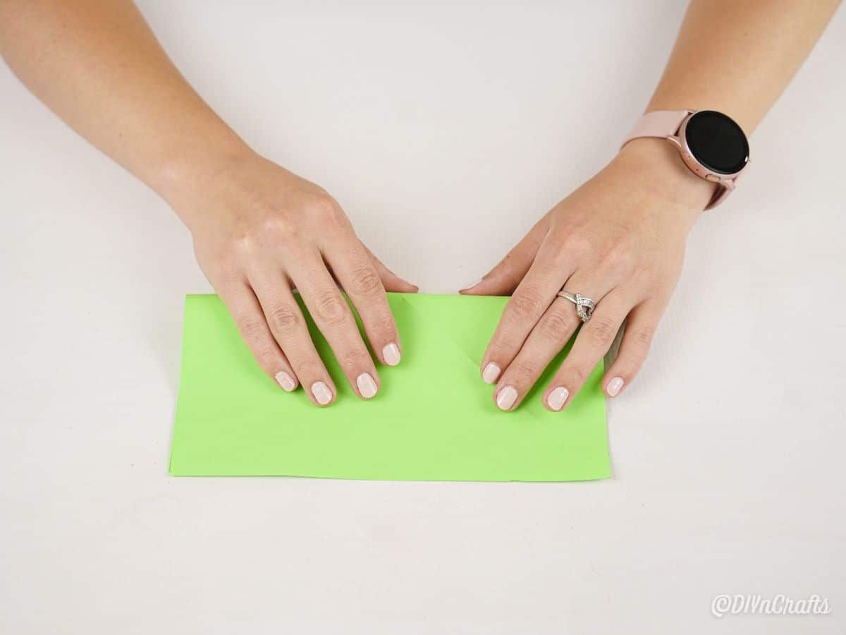 руки складывают зеленую бумагу пополам