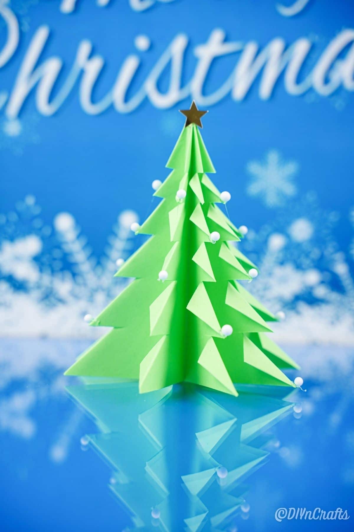 бумажная 3d рождественская елка на синей поверхности с искусственным снежным фоном