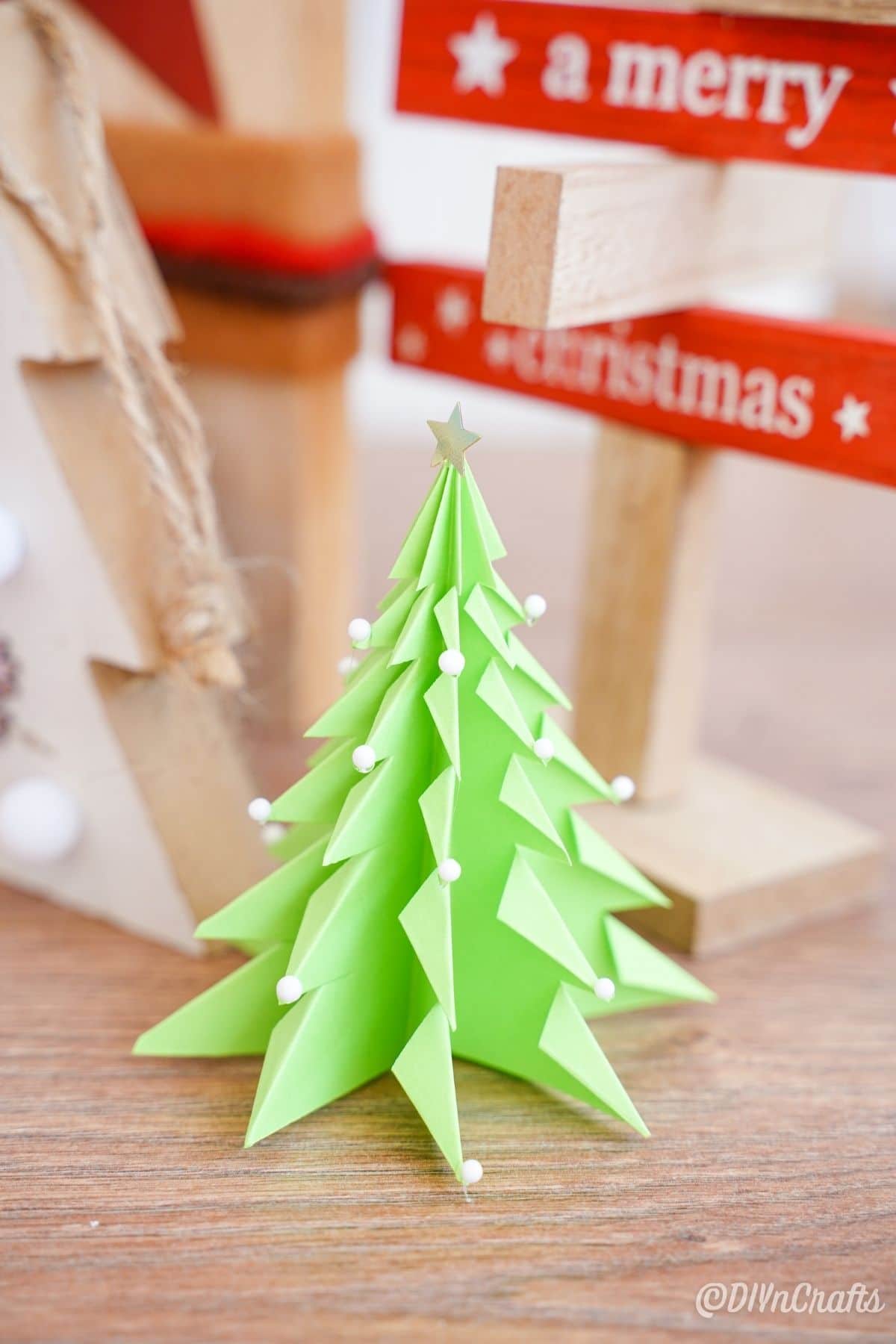 бумажная 3d рождественская елка на столе с деревянным знаком
