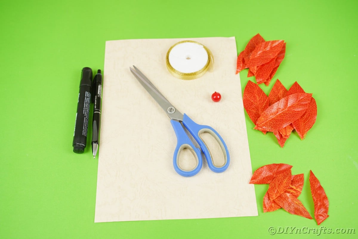 Кремовые ножницы для бумаги и оранжевые поддельные листья на зеленой поверхности