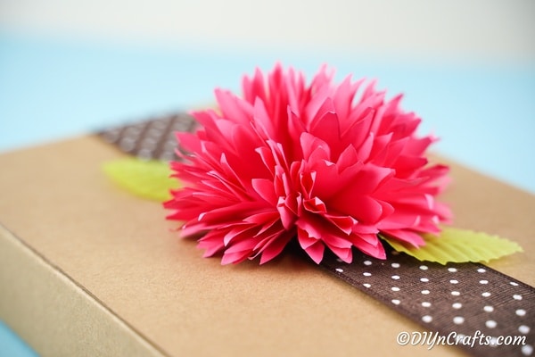 Розовый бумажный цветок поверх коричневой картонной коробки