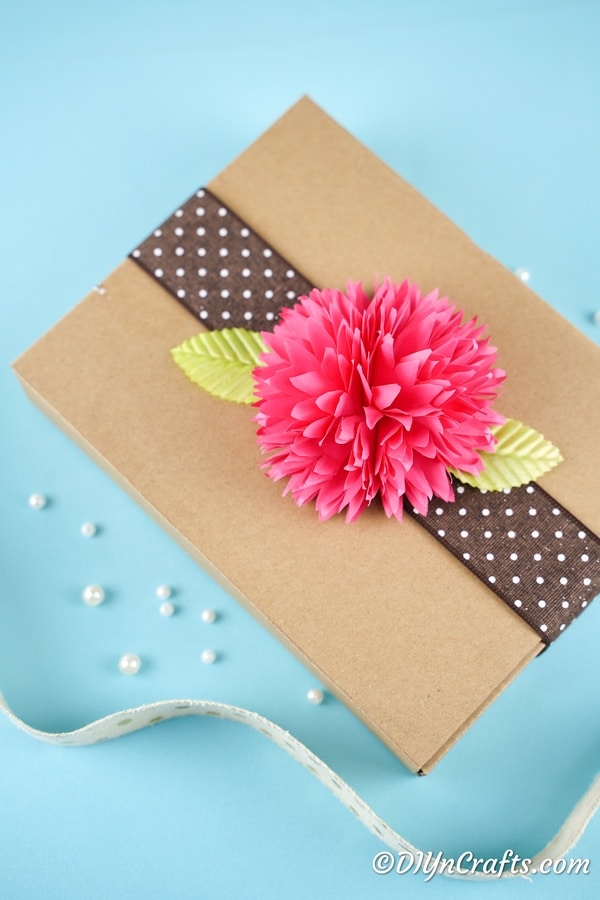 Розовый бумажный цветок поверх коричневой коробки в качестве декора подарка