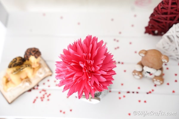 Бумажный цветок на белом столе с конфетти