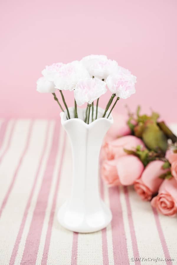 Бумажные цветы в белой вазе на розовом столе