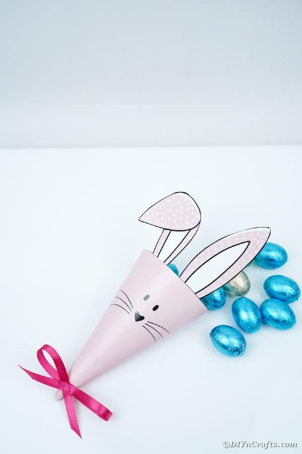 Бумажный конус кролика на белом столе с синими конфетами