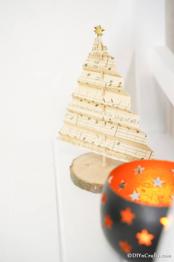 Новогодняя елка из нотной бумаги на мантии рядом с маленькой свечой.