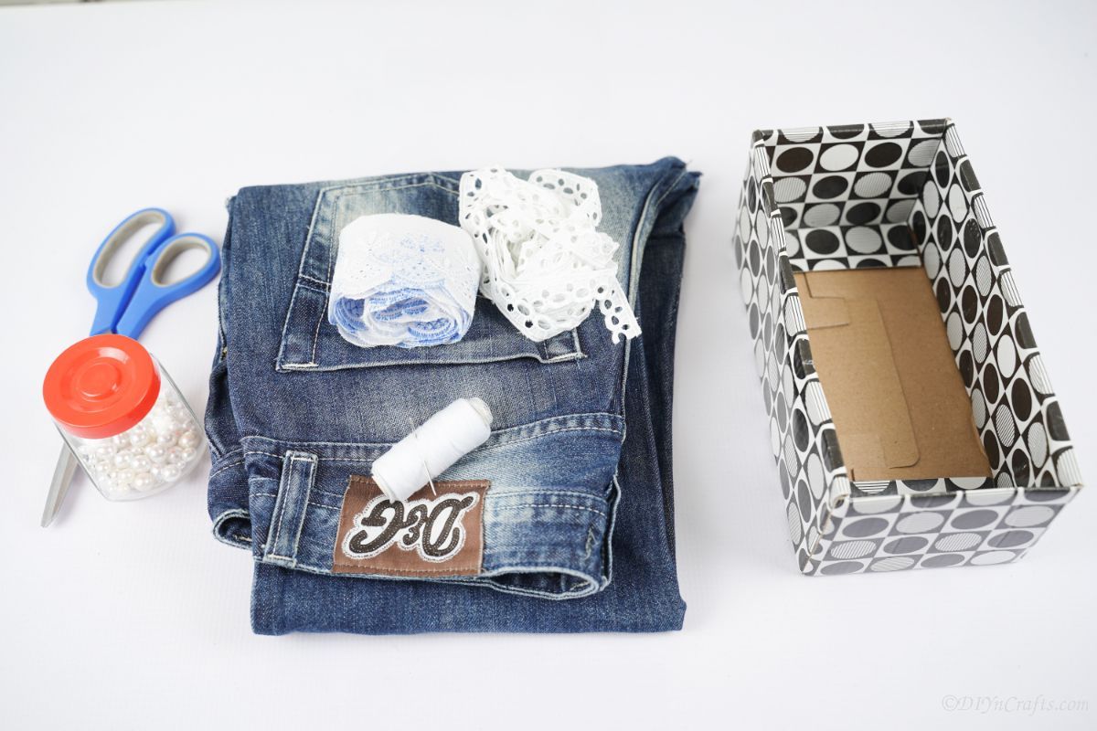 коробка на столе рядом со сложенными синими джинсами, рулоном кружева и ножницами