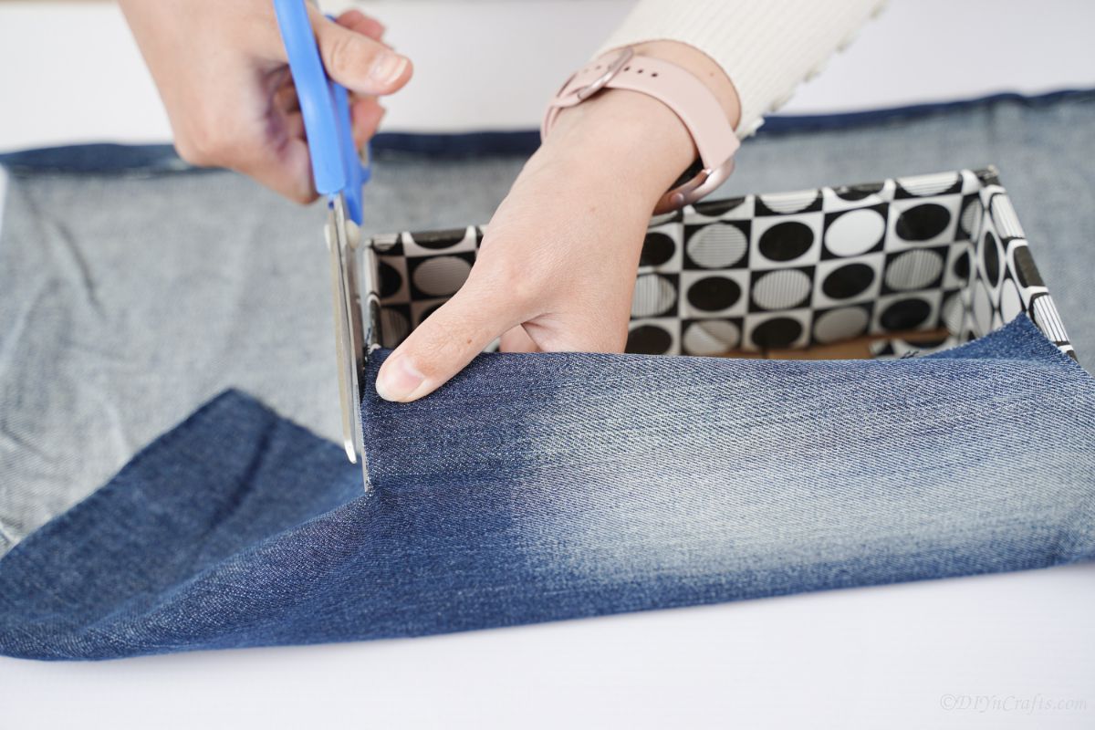 синие ножницы обрезают лишнюю джинсовую ткань вокруг коробки