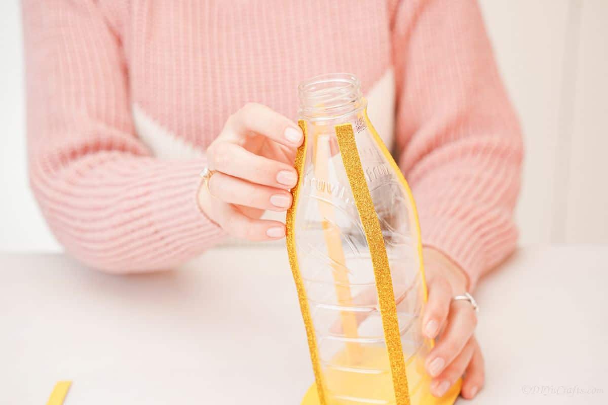 рука держит золотую блестящую бумагу против пластиковой бутылки