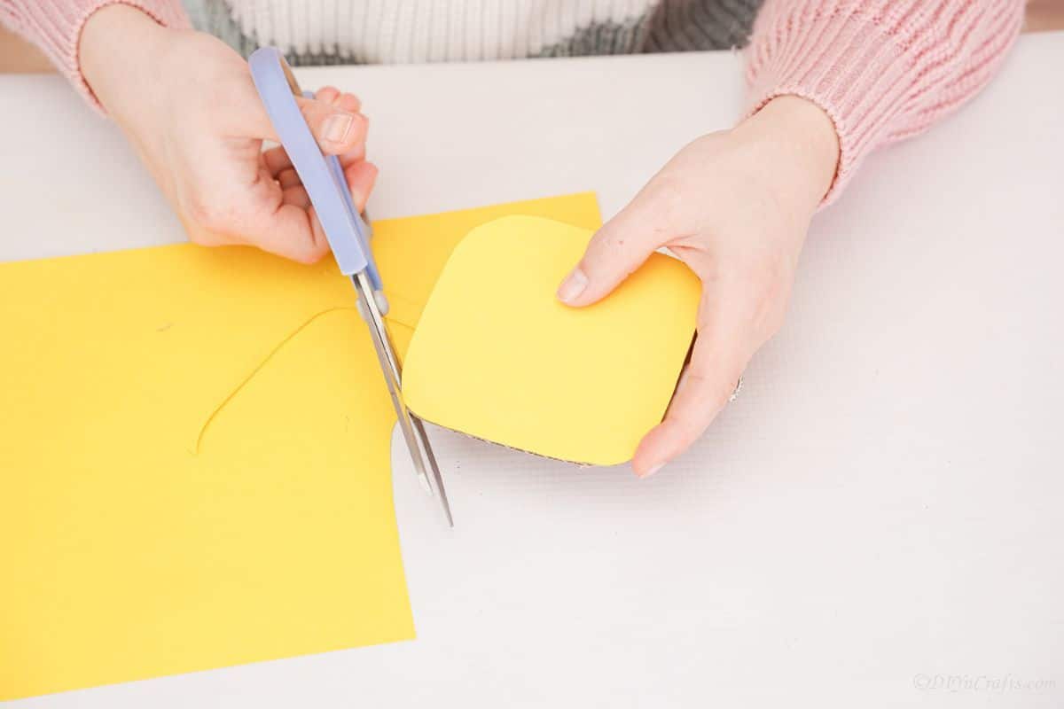 синие ножницы обрезают желтую бумагу до закругленного квадрата